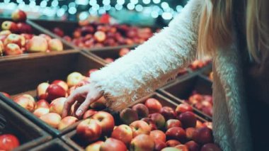 Kadın elleri süpermarketteki tahta kutulardan elma alıyor.