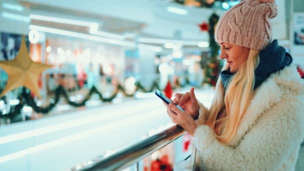 Uma mulher loira fica em um supermercado e olha para um smartphone em busca de compras — Vídeo de Stock