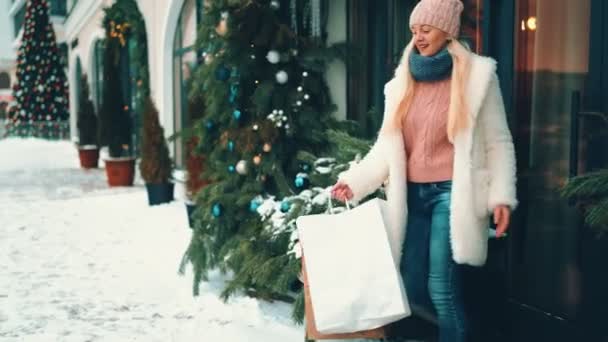 Mulher loira saindo da loja segurando compras na rua perto da loja decorações de Natal — Vídeo de Stock