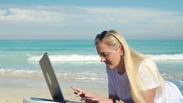美しい砂浜でお金を稼ぐビジネスの成功した女性は仕事や旅行をしています かわいいですブロンドモデルノートブックやノートパソコンでリラックス休暇の笑顔人生を楽しんで — ストック動画