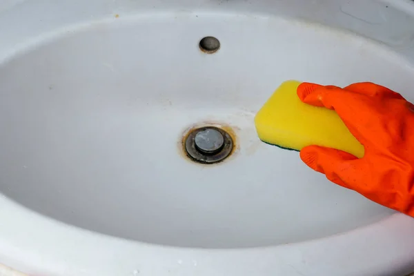 Person hand holding a yellow sponge and cleans a dirty sink in rust, Clean dirty sinks. Homework concept.
