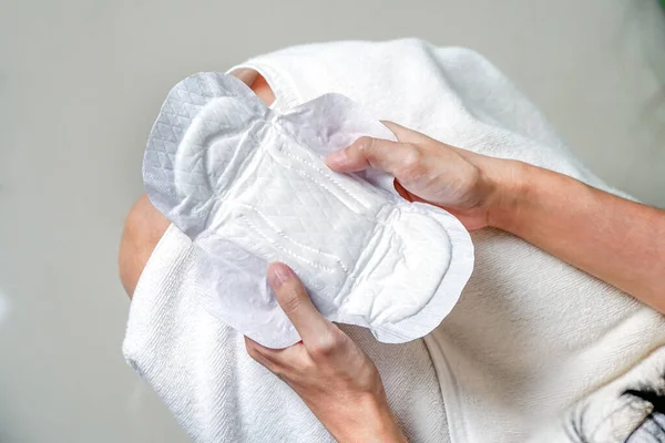 woman wearing a towel holding a sanitary napkin or menstruation pad before wearing it. Women using it during menstruation to avoid damage to clothing.