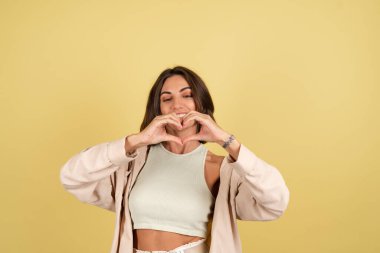 Sarı arka plandaki kadının kapalı stüdyo portresi mutlu, neşeli elleri olan bir kalp.