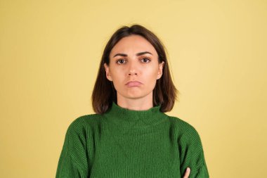Yeşil, sıcak süveterli, ciddi odaklanmış, mutsuz, kolları bağlı genç bir kadın.