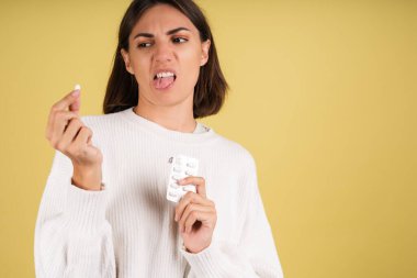 Beyaz kazak giyen, hap alan genç bir kadın hasta olduğu için hayal kırıklığına uğramış ve mutsuz.