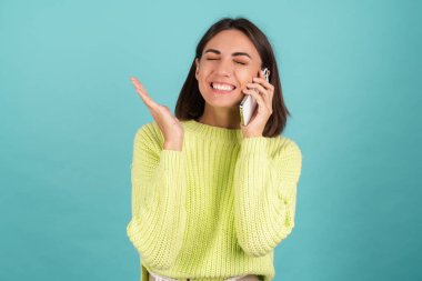 Açık yeşil kazaklı genç bir kadın cep telefonuyla konuşuyor. Sesli mesaj dinliyor. Mutlu bir kazanan var.