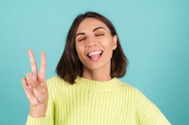 Açık yeşil kazaklı, sevimli, gülümseyen V işaretli genç kadın.