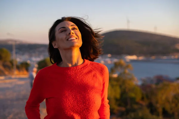 ロマンチックな気分の背景に山の壮大な夕日で赤いセーターの若い女性は 喜んで笑顔 — ストック写真