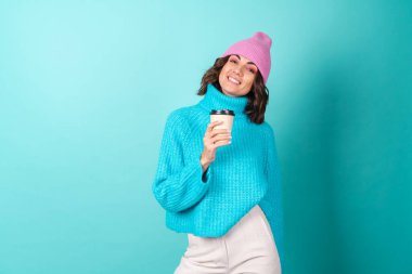 Mavi süveter ve elinde bir fincan sıcak kahve tutan parlak makyajlı pembe şapkalı genç bir kadının samimi portresi.