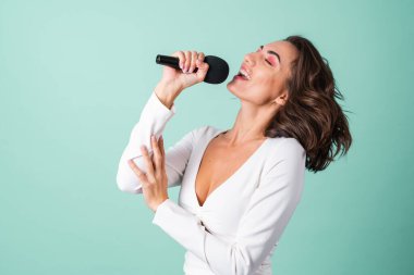 Açık yeşil arka planda açık yeşil elbiseli genç bir kadın açık pembe makyajlı elinde bir mikrofon, karaoke söylüyor.