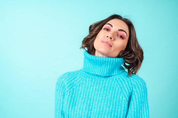 Cozy portrait of a young woman in a knitted blue sweater and bright pink makeup on a turquoise background