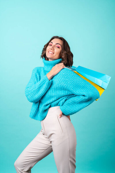 Уютный портрет молодой женщины в трикотажном голубом свитере и ярко-розовый макияж на бирюзовом фоне с сумками для покупок