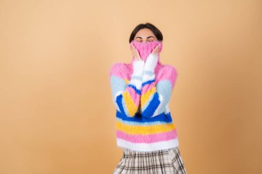 Bej arka planda, parlak renkli, rahat örgü süveter ve güzel gülümseyen ekose etekli genç bir kadın.