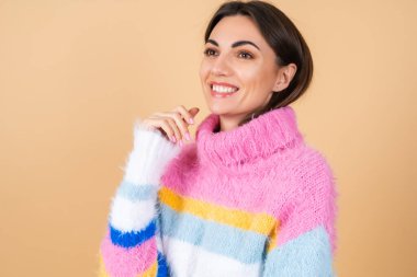 Bej arka planda, parlak renkli, rahat örgü süveteri olan genç bir kadın gülümsüyor.