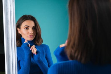 Mavi balıkçı yaka giyen, golf oynayan, aynanın önünde şehvetle poz veren genç bir kadın.