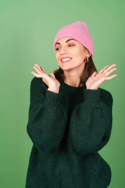 若いです女性で緑の背景に暖かい居心地の良いセーターとピンクの帽子かわいい笑顔 — ストック写真
