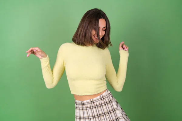 黄色のセーターと遊んだスカートの中の緑の背景に若い女性はかわいい笑顔 良い上品な雰囲気の中で動きます — ストック写真