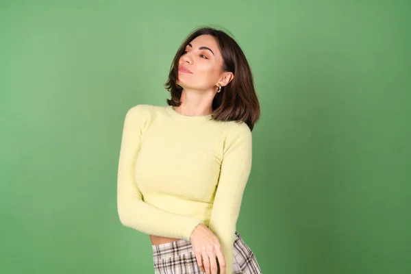 Young Woman Green Background Yellow Sweater Plaid Skirt Smiles Cutely — Stock Photo, Image