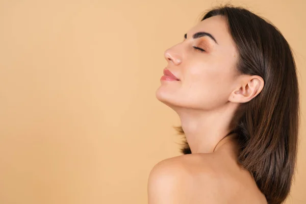 Bej bir arka planda, doğal makyajlı, açık tenli, çıplak omuzlu, güzel yüzlü, kozmetik ve bakım reklamları yapan genç bir kızın portresi.
