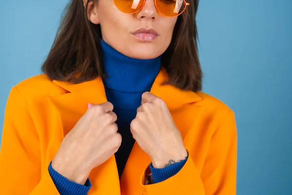 膝丈でオーバーサイズのジャケットを着たファッショナブルな若い女性に青の背景にスタイリッシュな明るいオレンジ色のメガネポーズ — ストック写真