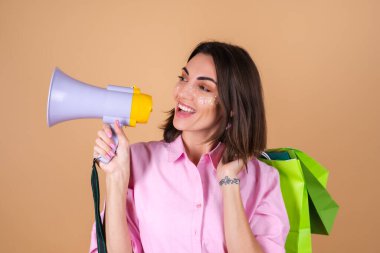 Bej bir arka planda pembe elbiseli genç bir kadının portresi. Parlak makyajlı. Elinde alışveriş paketleri var.