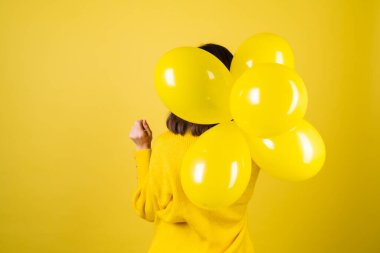 Sarı kazaklı bir kızın sırtındaki çerçeve. Elinde balonlar, neşeli bir ruh hali. Doğum günü partisi beklentisi.