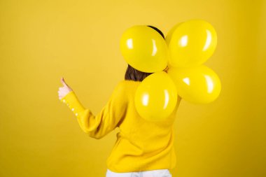 Sarı kazaklı bir kızın sırtındaki çerçeve. Elinde balonlar, neşeli bir ruh hali. Doğum günü partisi beklentisi.