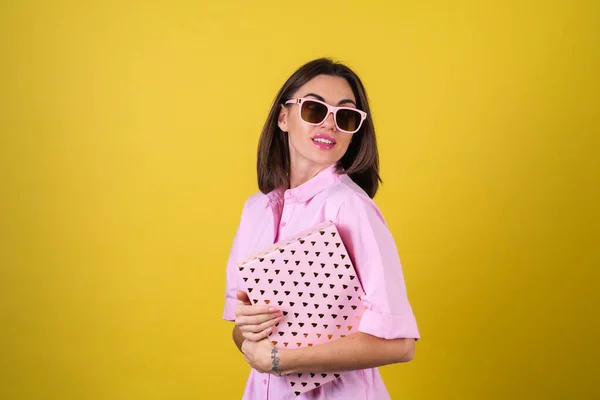 时尚的年轻女性穿着粉色衣服 戴着黄色背景的眼镜 手里拿着礼品盒 庆祝情人节最美好的节日 — 图库照片