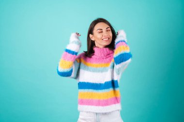 Mavi arka planda parlak renkli bir süveter giyen genç bir kadın coşkuyla gülüyor, başını çeviriyor, saçları uçuşuyor, gözleri kapalı.