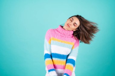 Mavi arka planda parlak renkli bir süveter giyen genç bir kadın. Gözleri kapalı gülümseyen, pürüzsüz saçlı, güzel uçan, dolgun dudaklı, çıplak makyajlı.