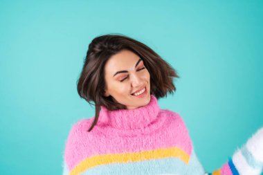 Mavi arka planda parlak renkli bir süveter giyen genç bir kadın. Gözleri kapalı gülümseyen, pürüzsüz saçlı, güzel uçan, dolgun dudaklı, çıplak makyajlı.