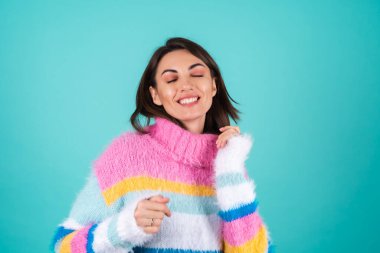 Mavi arka planda parlak renkli bir süveter giyen genç bir kadın, gülümsüyor, neşeyle hareket ediyor, tek başına dans ediyor.