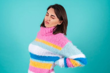 Mavi arka planda parlak renkli süveter giyen genç kadın sırt ağrısından muzdarip.