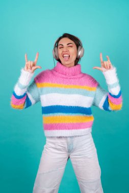 Mavi arka planda parlak renkli bir süveter giyen, kulaklıkları iptal eden, en sevdiği müzikle eğlenen, müzik seven genç bir kadın.