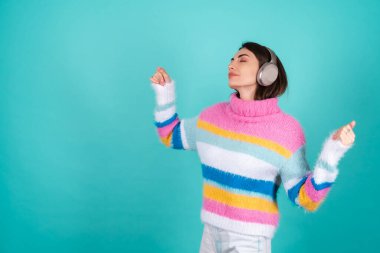 Mavi arka planda parlak renkli bir süveter giyen, kulaklıkları iptal eden, en sevdiği müzikle eğlenen, müzik seven genç bir kadın.