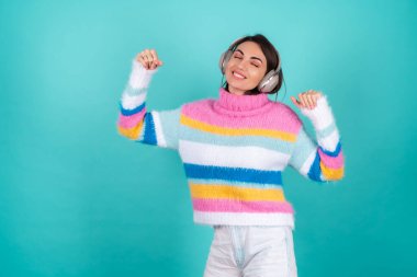 Mavi arka planda parlak renkli bir süveter giyen, kulaklıkları iptal eden, en sevdiği müzikle eğlenen, müzik seven genç bir kadın.