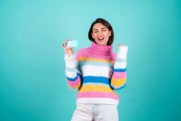 青の背景に明るい多色のセーターの若い女性は クレジットカードを示して 幸福とジャンプ 非常に満足している 勝者のジェスチャー — ストック写真