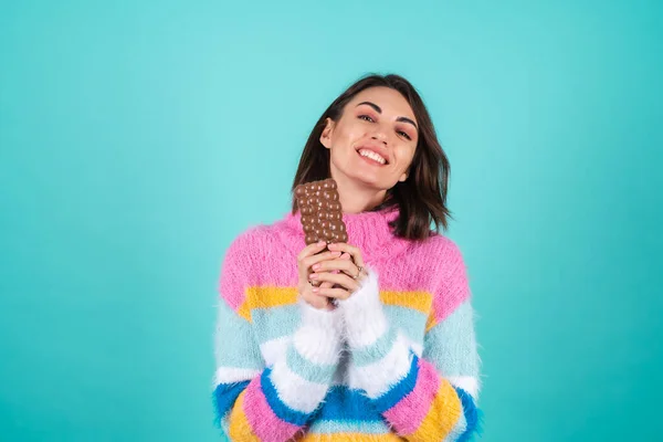 青を基調とした明るいマルチカラーのセーターを着た若い女性は おいしいミルクチョコレートのすべての部分を楽しんでいます — ストック写真