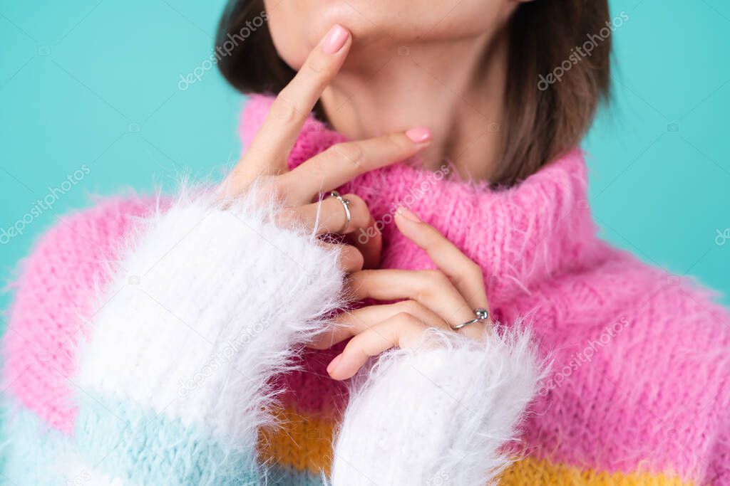 Close portrait of a young woman in a sweater on a blue background with graceful hands, long thin fingers, two cute silver rings, plump nude lips