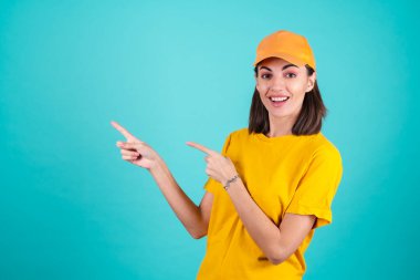 Genç kadın teslimatçı, kurye, mavi arka planda bir şapka, geniş gülümseme ve sol parmakla işaret