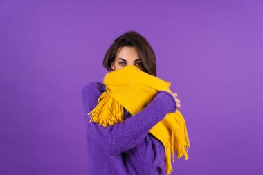 Young woman in purple soft cozy sweater and yellow scarf with makeup posing in studio