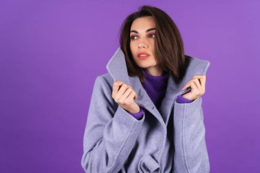 Young woman in a gray coat on a purple background posing, cozy and warm, autumn winter style
