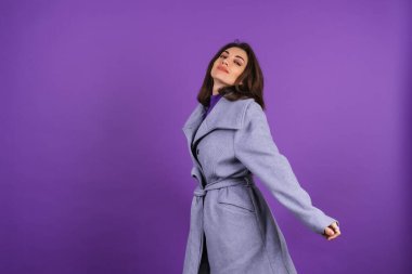 Young woman in a gray coat on a purple background posing, cozy and warm, in an autumn-winter style, the girl smiles cheerfully