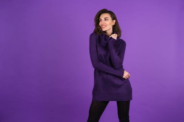 Young woman in a knitted warm dress and black tights on a purple background, beautiful figure, smiling cheerfully