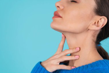 Young woman in a blue knitted sweater and natural daytime makeup on a turquoise background, plump lips with nude matte lipstick