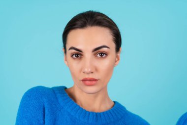 Beauty portrait of a young woman in a blue knitted sweater and natural day makeup, full lips with nude matte lipstick and perfect eyebrows, looks at the camera