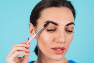 Beauty portrait young woman in a blue knitted sweater and natural day makeup, full lips with nude matte lipstick and perfect eyebrows, holds a brush