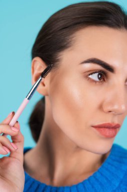 Beauty portrait young woman in a blue knitted sweater and natural day makeup, full lips with nude matte lipstick and perfect eyebrows, holds a brush