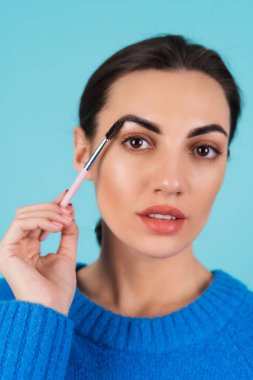 Beauty portrait young woman in a blue knitted sweater and natural day makeup, full lips with nude matte lipstick and perfect eyebrows, holds a brush