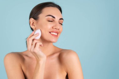 Close up beauty portrait of a woman with perfect skin and natural make-up, plump nude lips, holding a make-up sponge